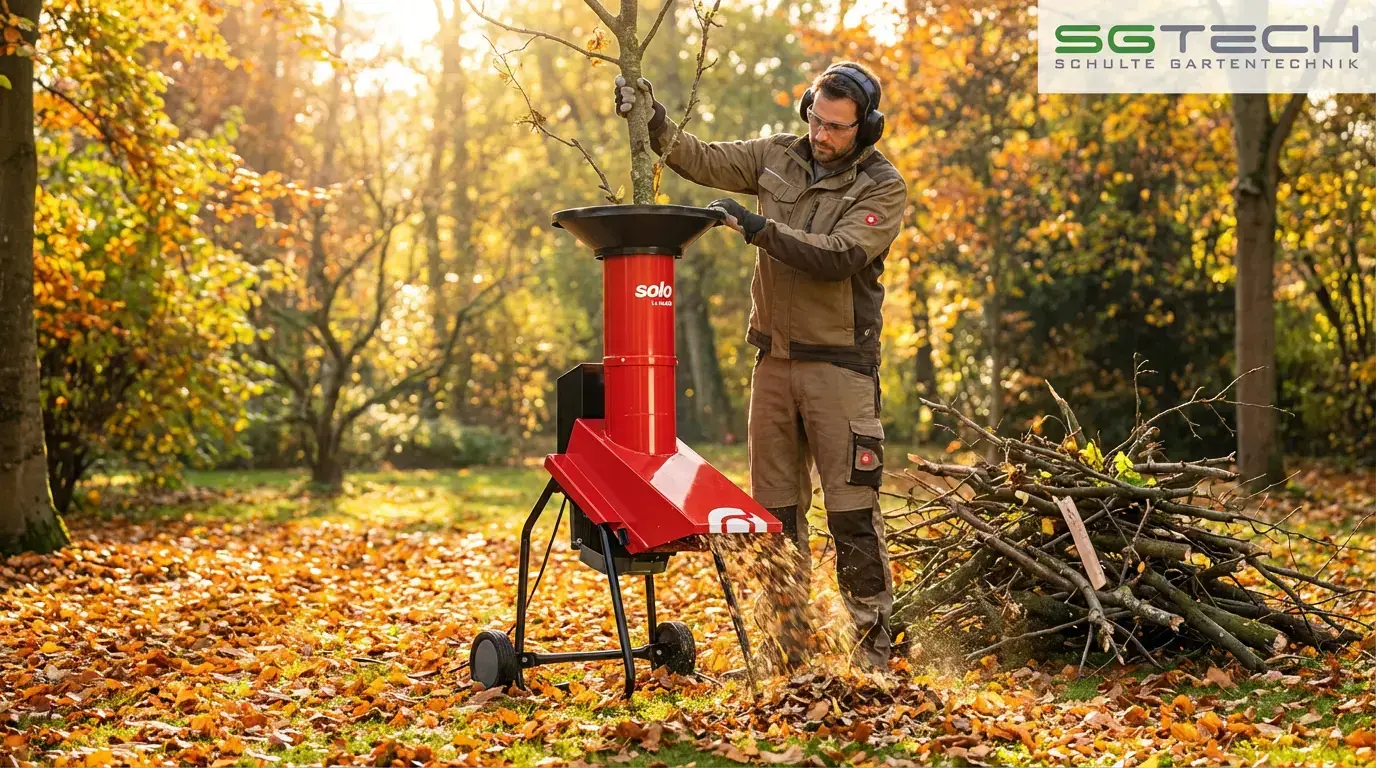 Ein Mann häckselt Äste mit dem roten Solo by AL-KO TCS DUOTEC 3000 Häcksler im herbstlichen Garten. Schnittgut fliegt aus dem Auswurf.