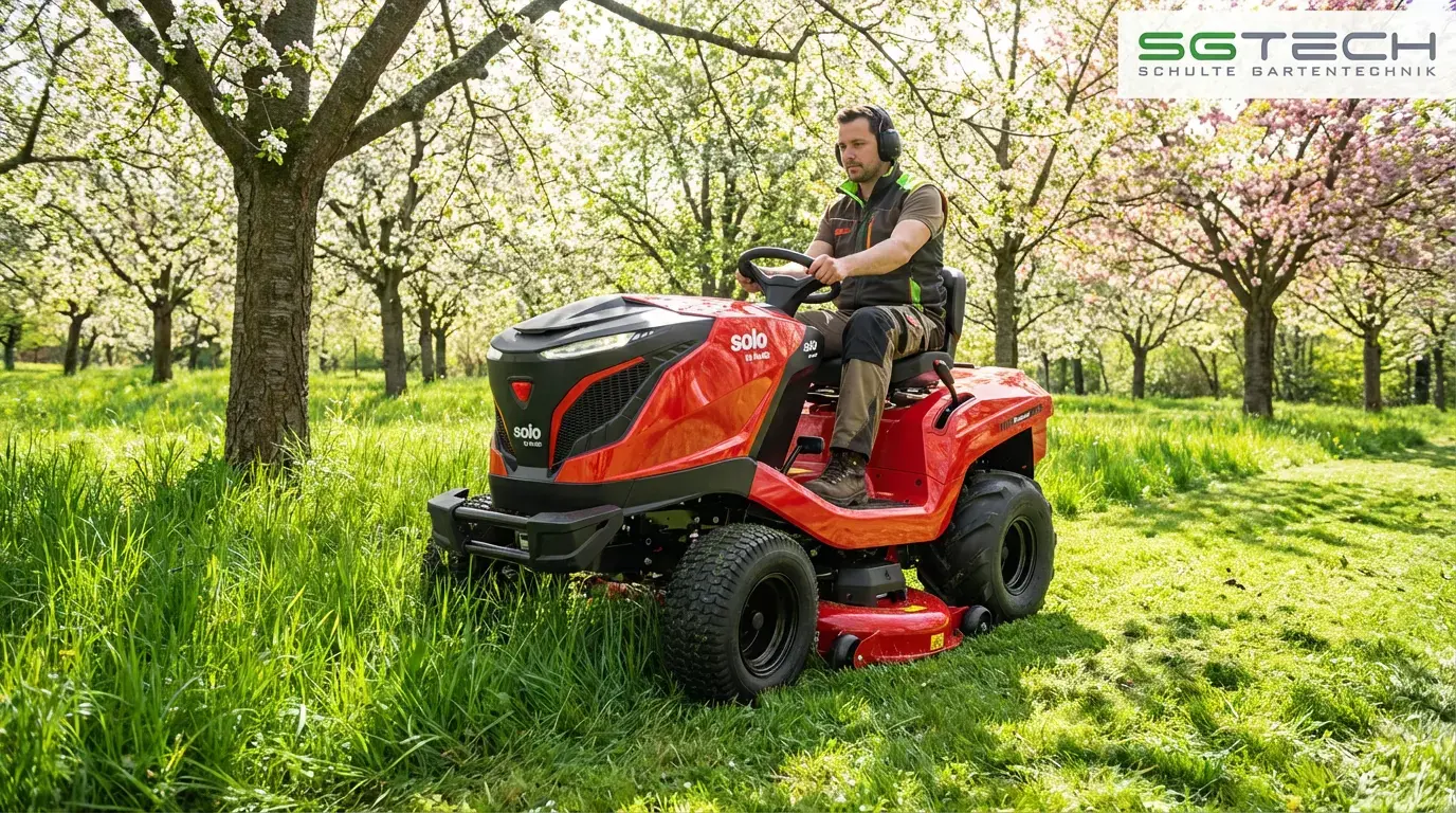 Mann fährt roten Solo by AL-KO T22-110.4HDH-A V2 Hochgrasmäher in einem blühenden Obstgarten, mäht hohes Gras im Frühling.