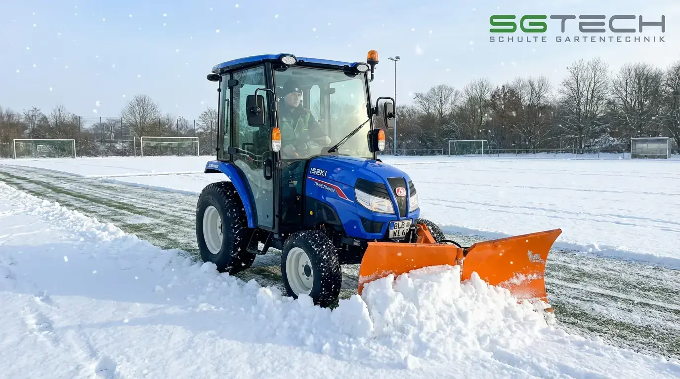 Iseki TM4270AHLK Traktor mit orangefarbenem Schneeschild räumt Schnee auf einem verschneiten Fußballplatz im Winter.