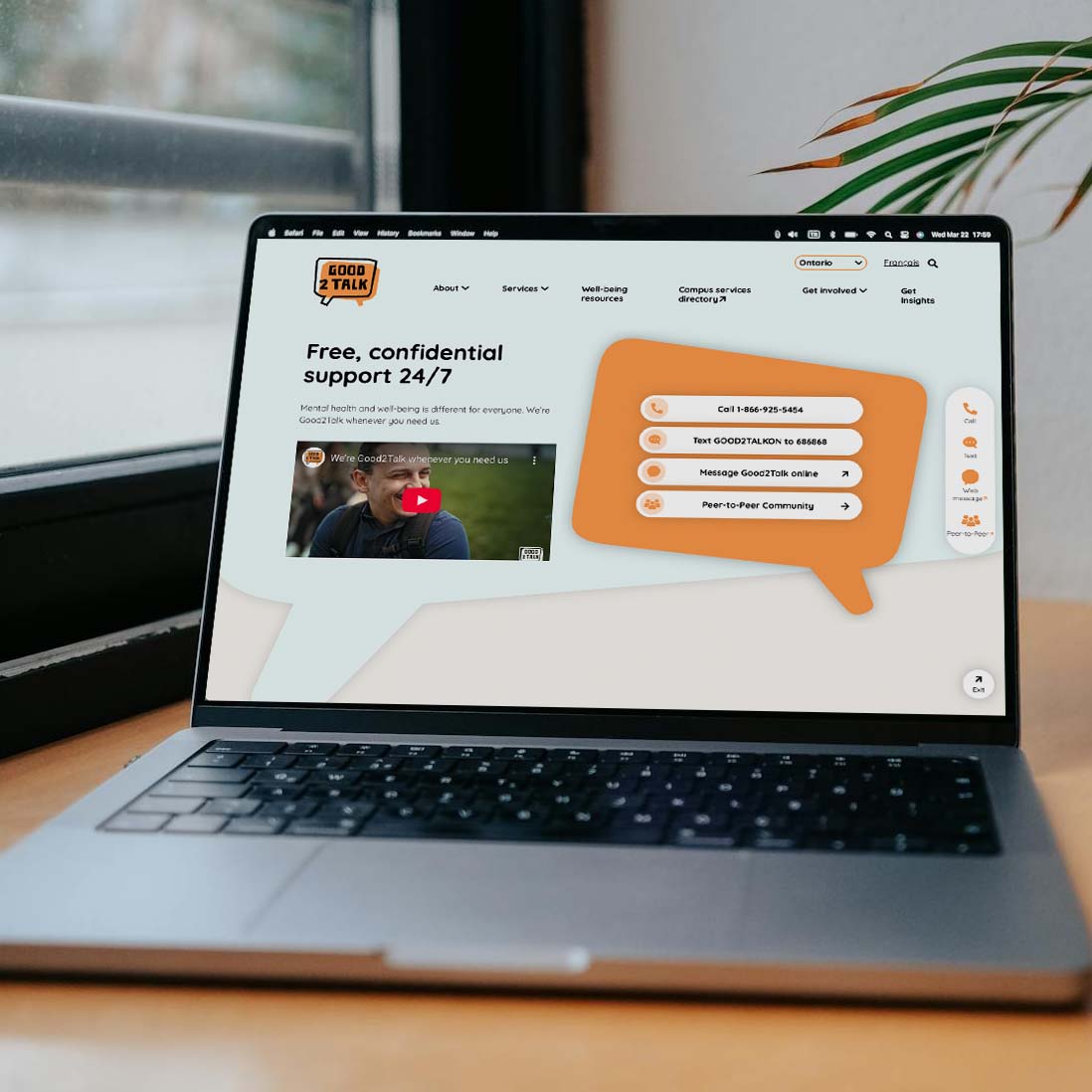 Laptop displaying Good2Talk website homepage offering free, confidential 24/7 mental health support with contact options and a video thumbnail.