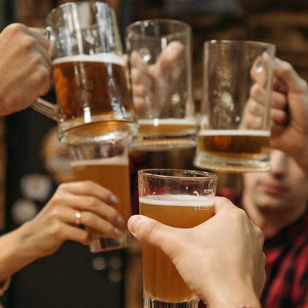 Group of people clinking beer glasses filled with amber beer in a celebration.