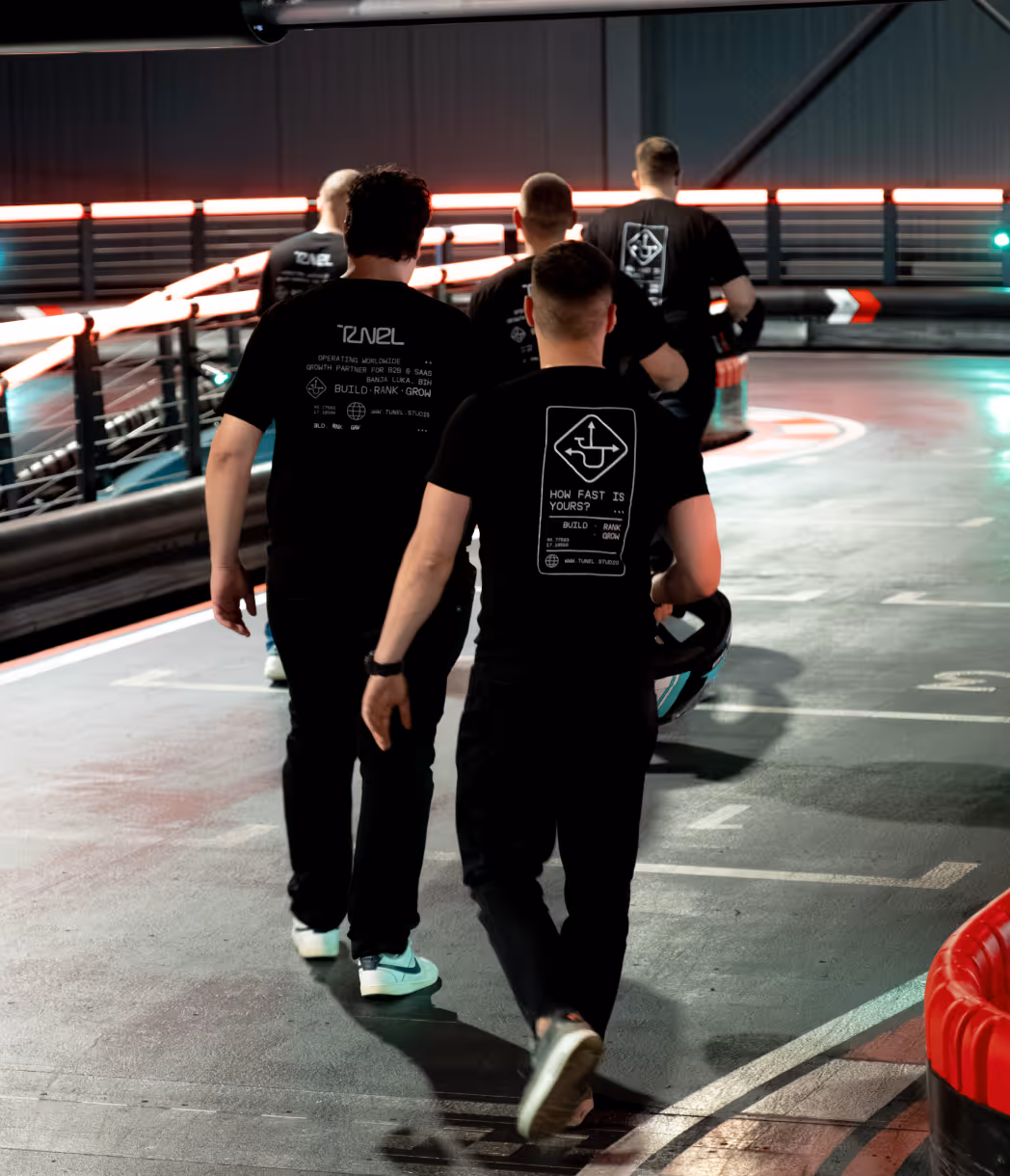 Four men wearing black Tunel Studio t-shirts walking on an indoor race track.