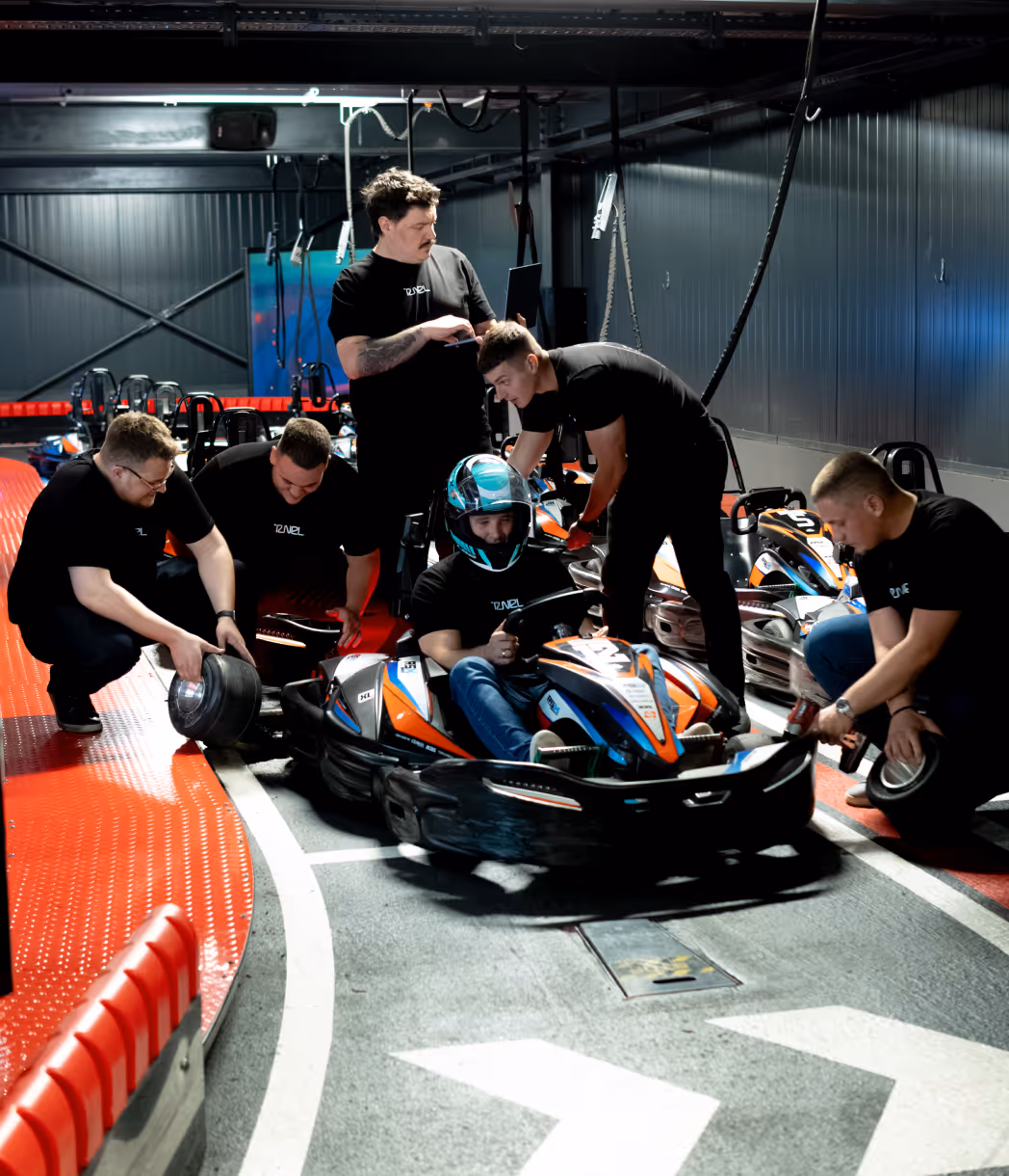 Crew in black shirts assisting a man wearing a helmet sitting in a go-kart at an indoor track.