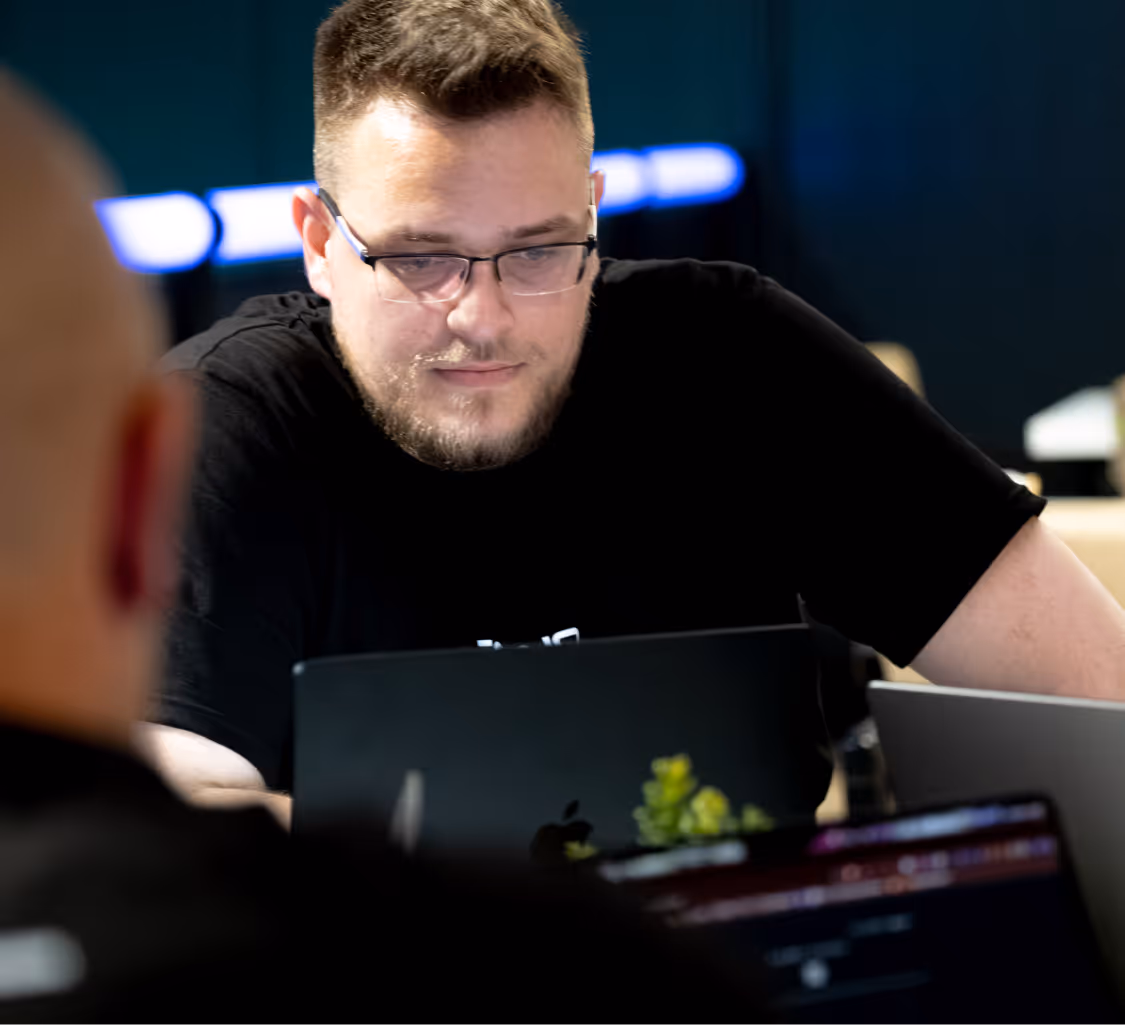 Man wearing glasses focused on a laptop screen in a dimly lit room.