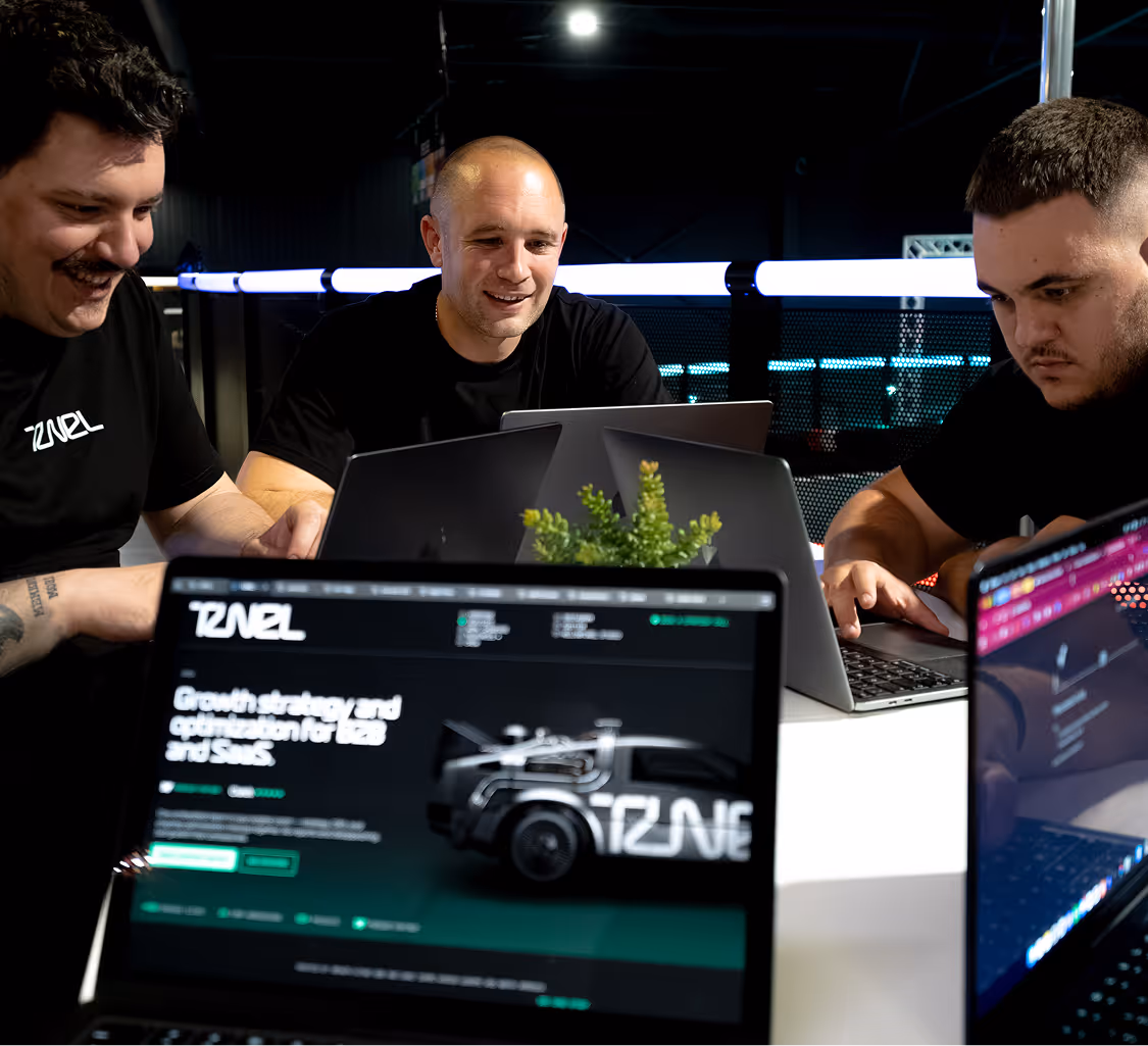 Three men working on laptops around a table with a small green plant in the center.