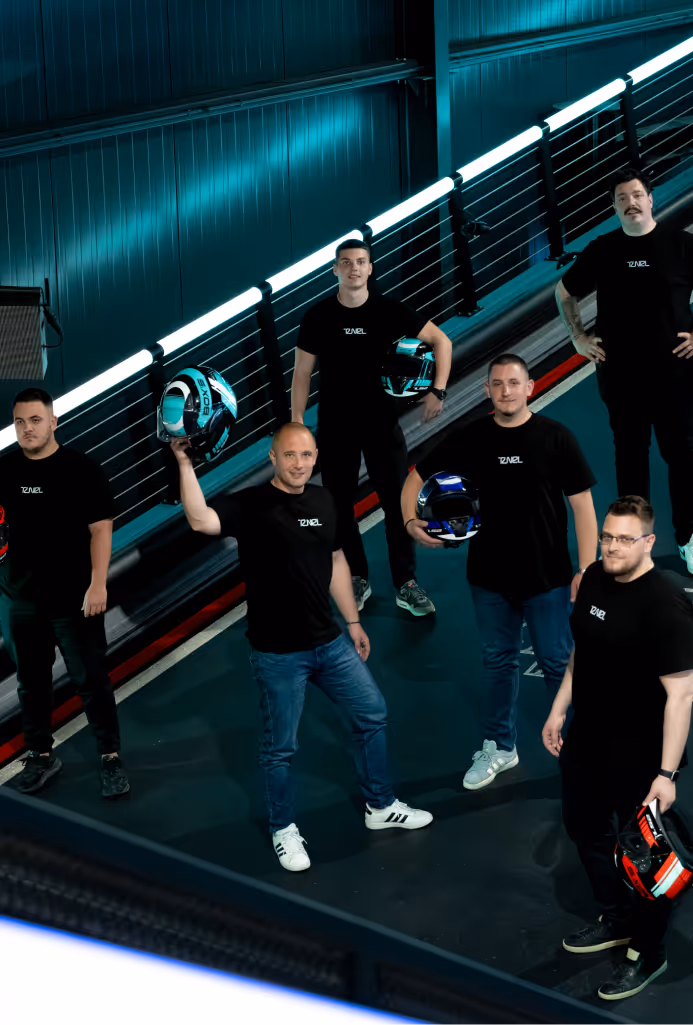 Group of six men in black t-shirts holding racing helmets in a dimly lit indoor venue.