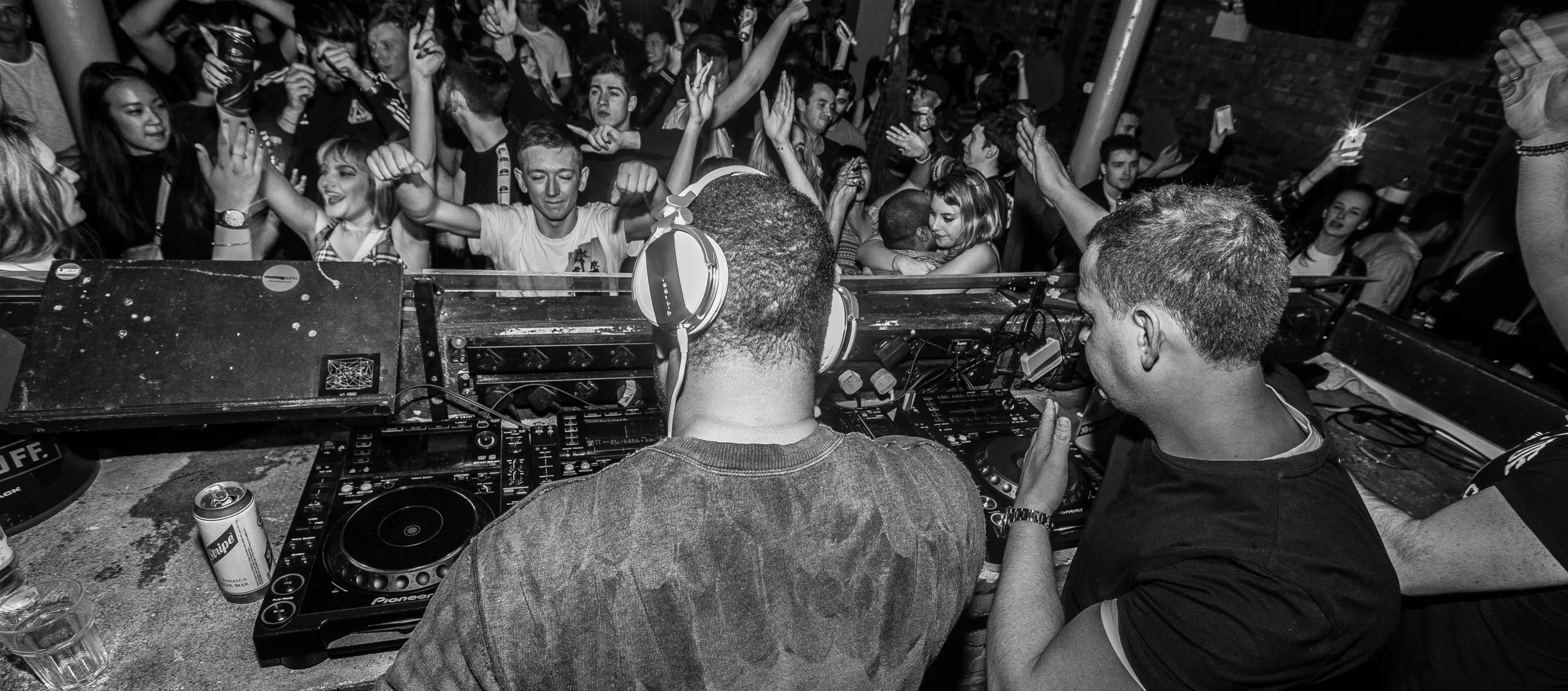 Two DJ course graduates perform in front of a massive crowd with hands in the air
