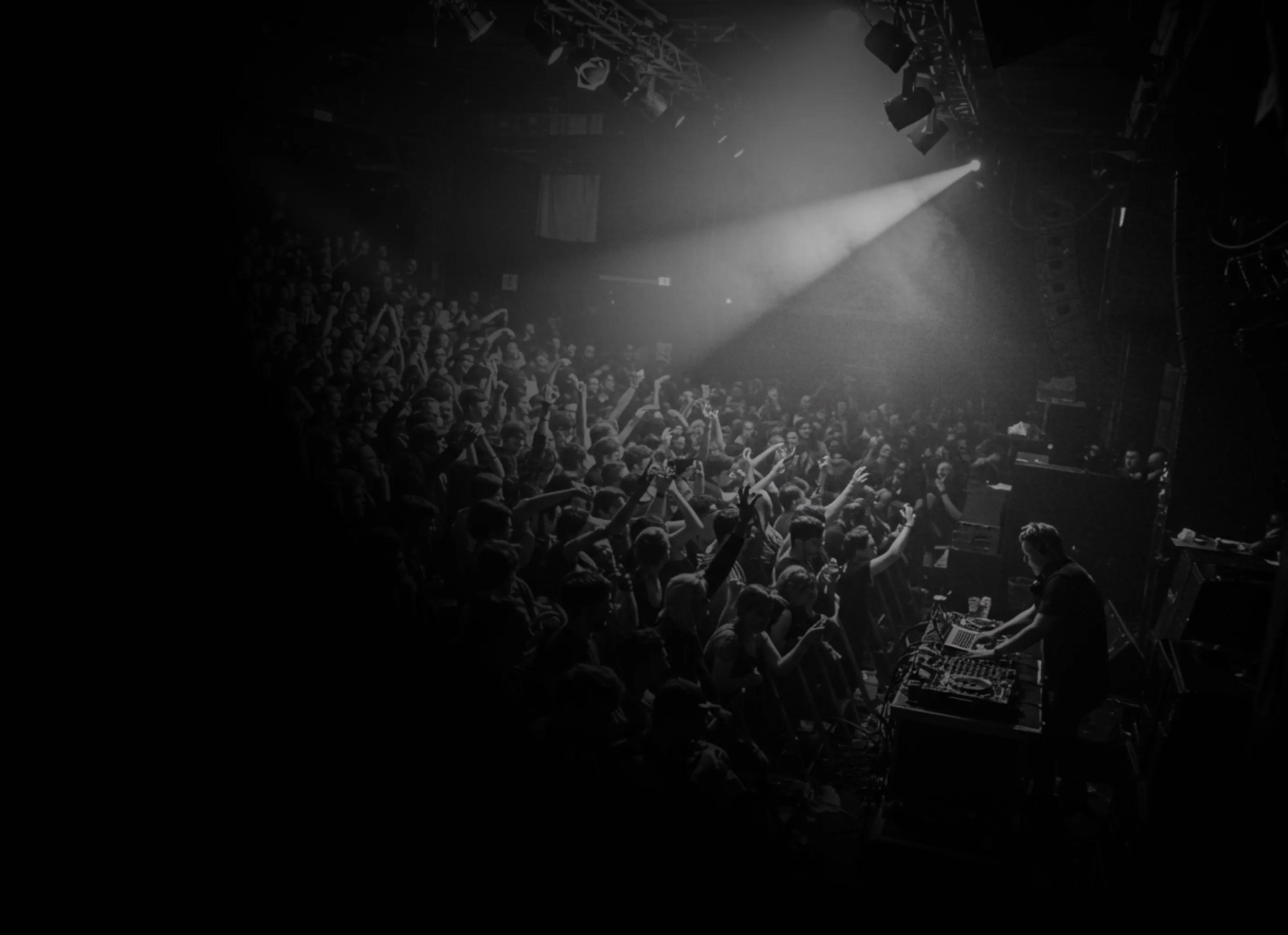 Crowd enjoying a live DJ performance under stage lights in a dark venue.