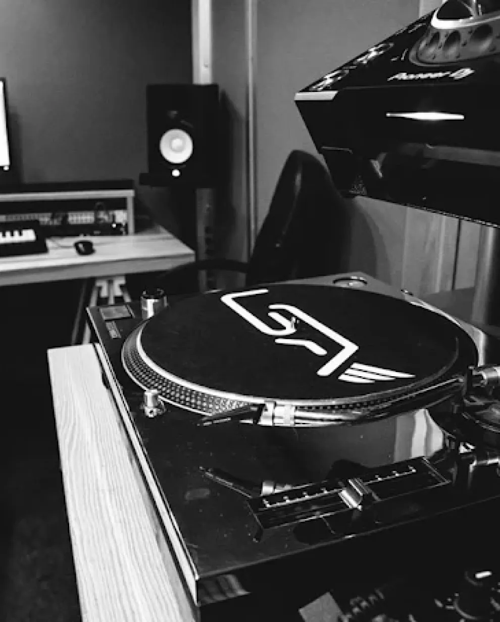 Close-up of a vinyl record player in a music studio with a speaker and keyboard in the background.