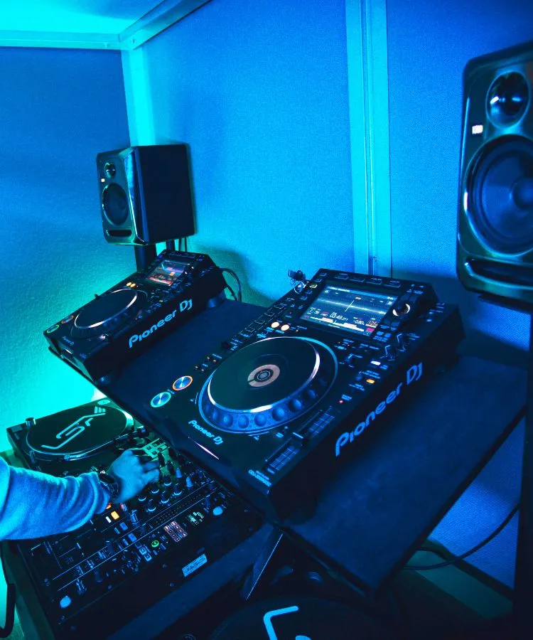 DJ setup with Pioneer DJ controllers and a speaker in a blue-lit room, with a person adjusting the controls.