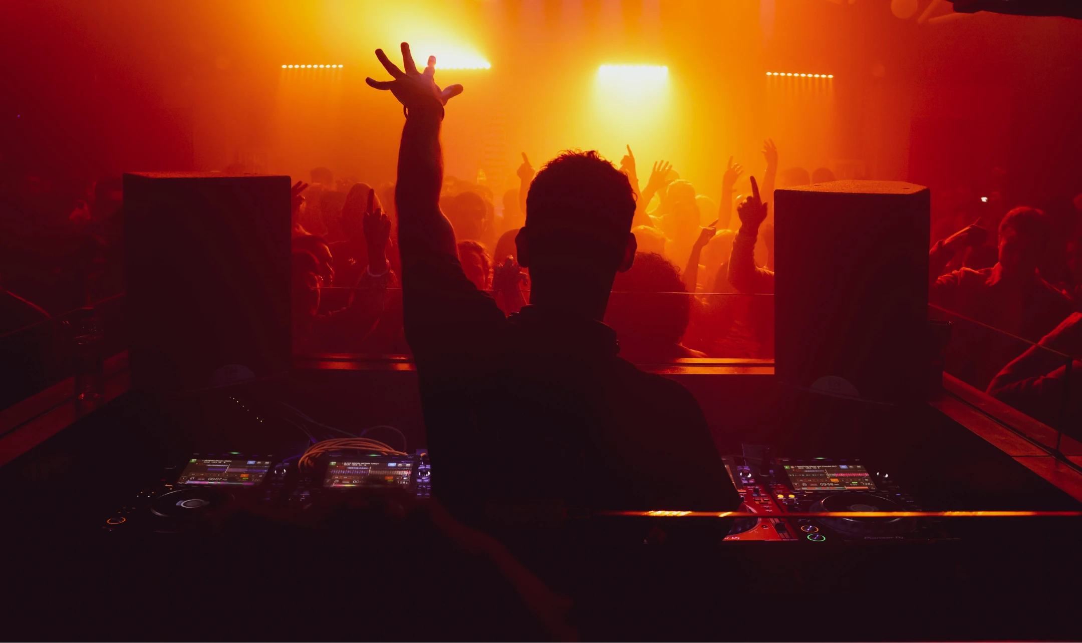 Two DJs mixing music on turntables and mixer equipment while a photographer takes pictures in a dimly lit club.