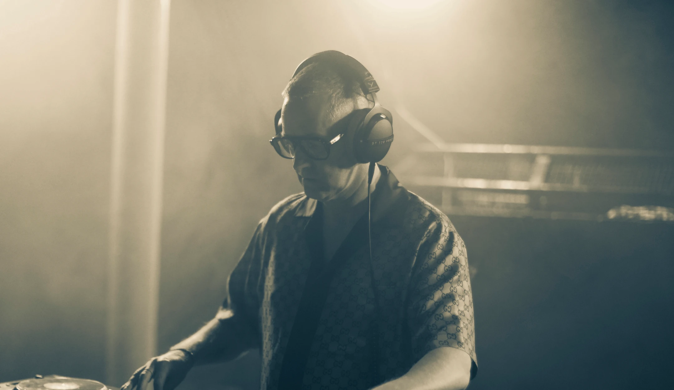 Hands of a DJ adjusting controls on a turntable mixer in a dark setting.