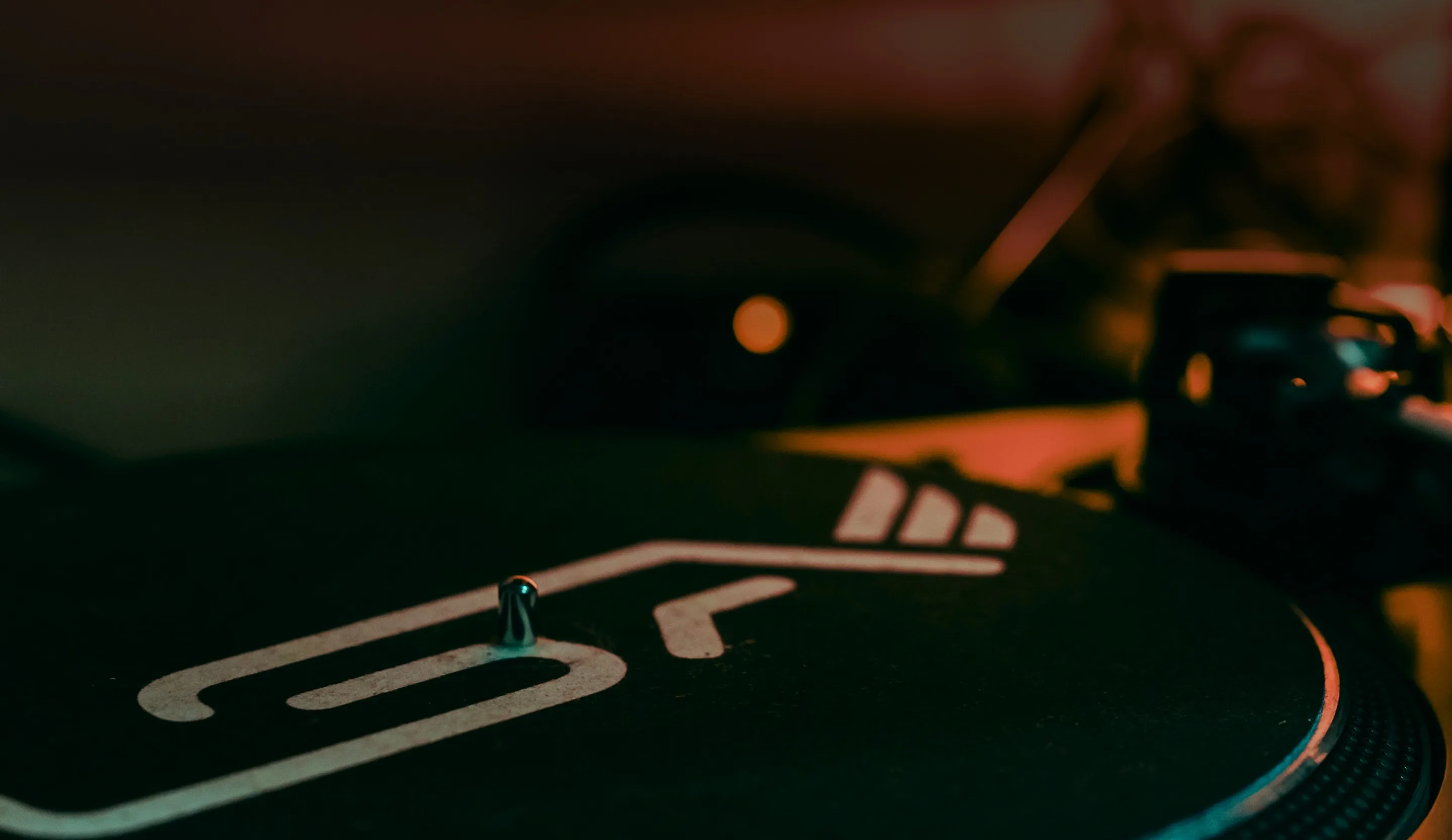 Close-up of a vinyl record player turntable with stylized white markings under warm low lighting.