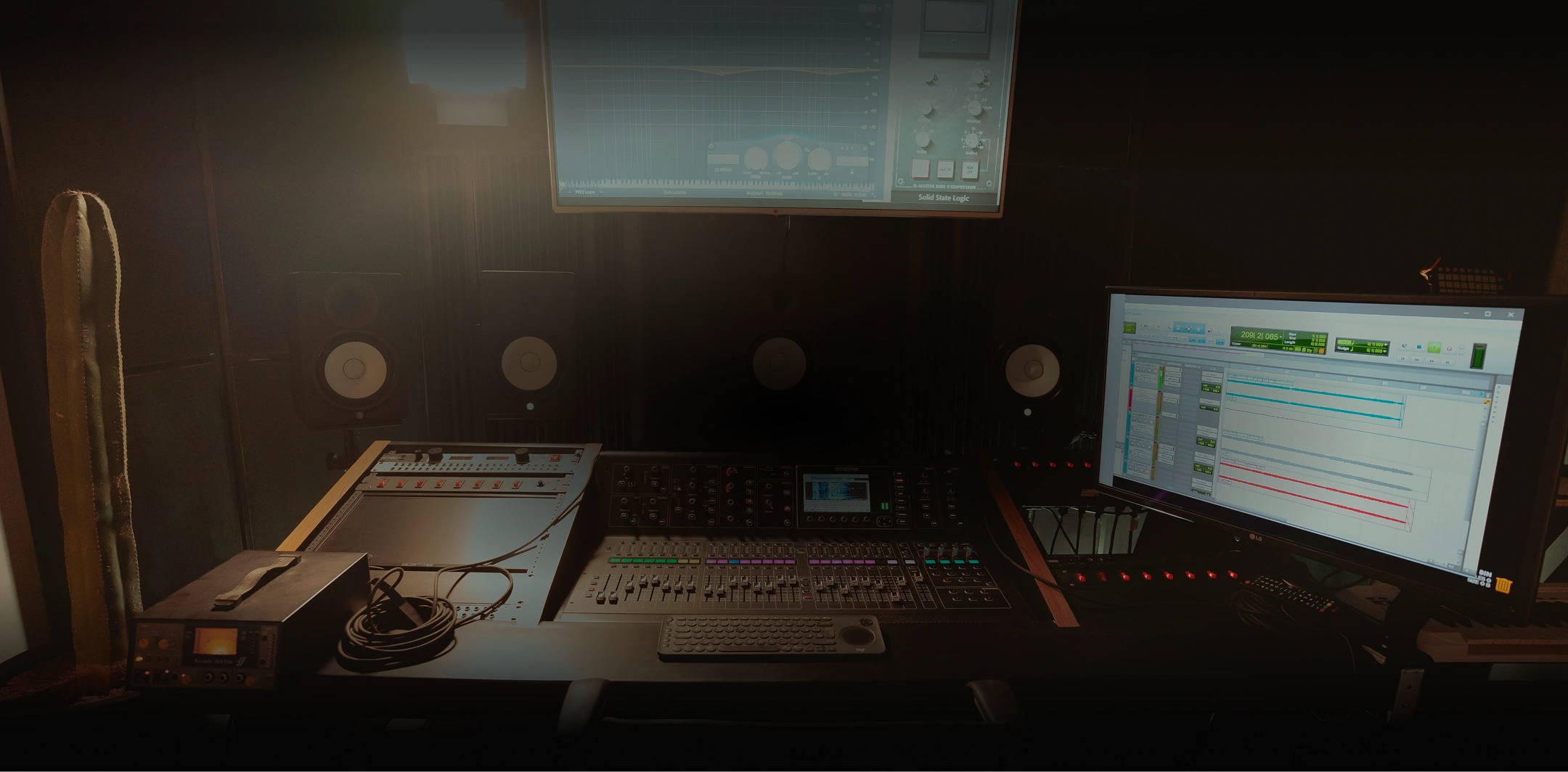 Dimly lit music production studio with mixing console, studio monitors, and computer screen displaying audio tracks.