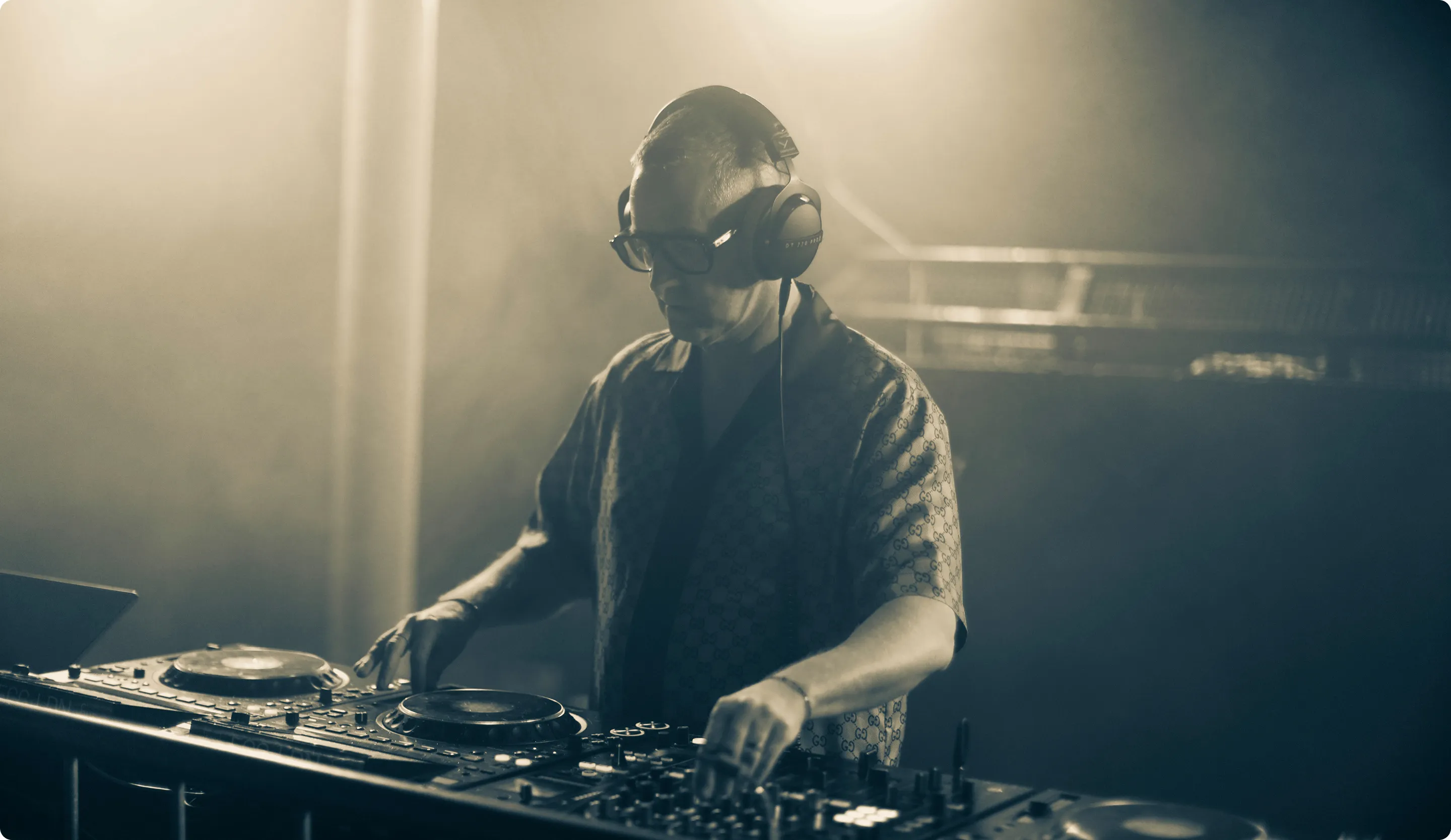 Hands of a DJ adjusting controls on a turntable mixer in a dark setting.
