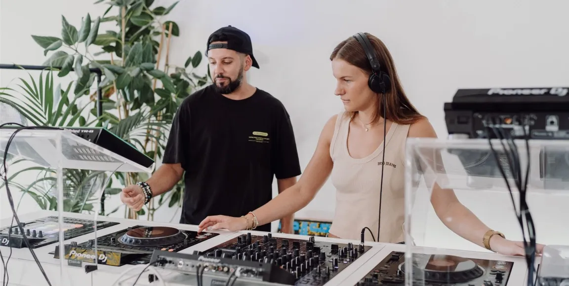A woman is learning how to DJ behind a professional DJ booth at London Sound Academy