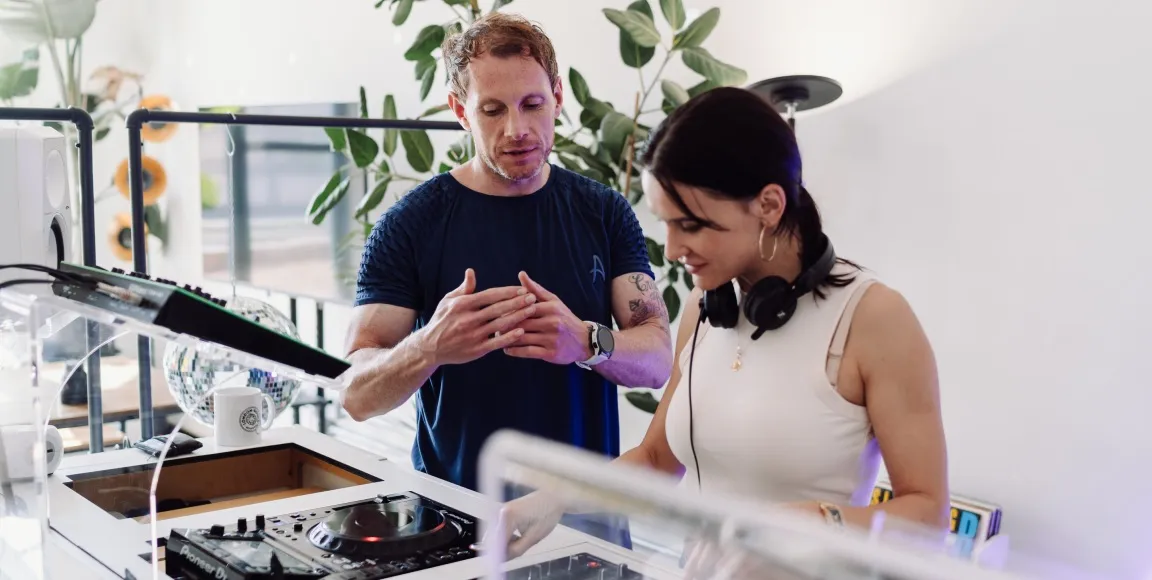 A woman is learning how to DJ behind a professional DJ booth at London Sound Academy