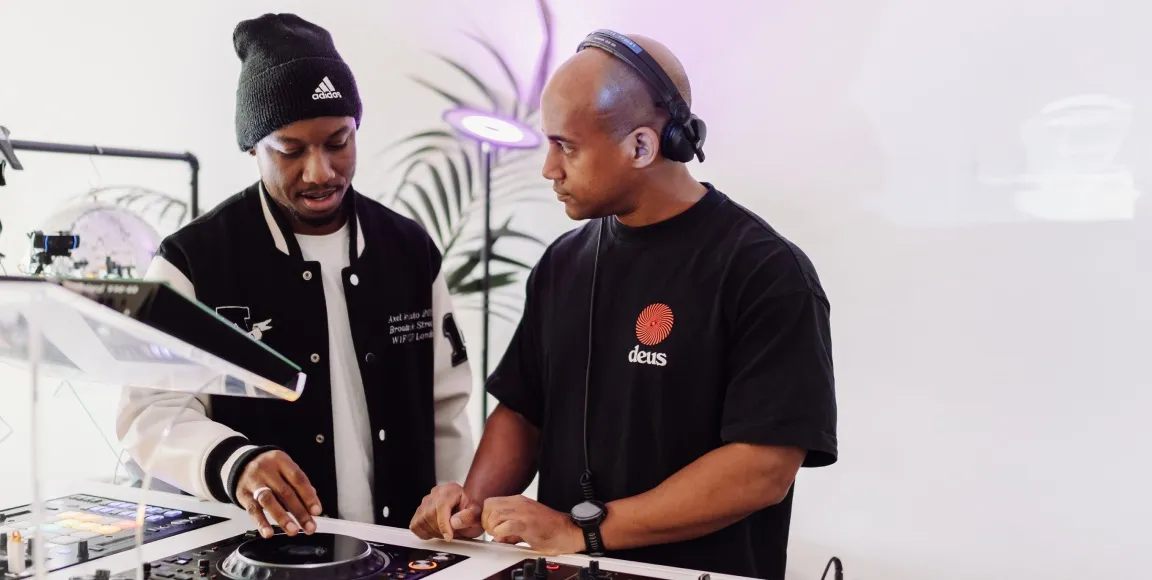 A woman is learning how to DJ behind a professional DJ booth at London Sound Academy