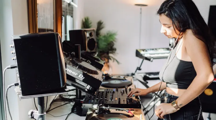 A woman is learning how to DJ behind a professional DJ booth at London Sound Academy