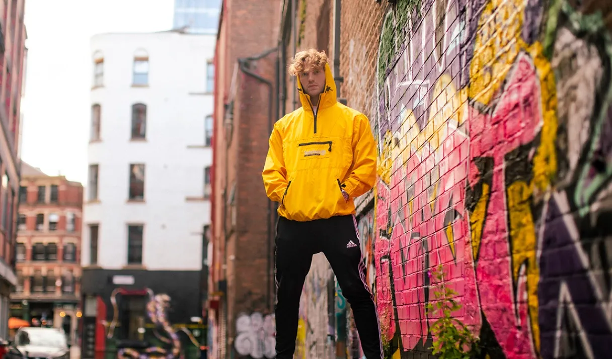 A stylish promotion photo of a DJ standing in a graffiti covered ally in London