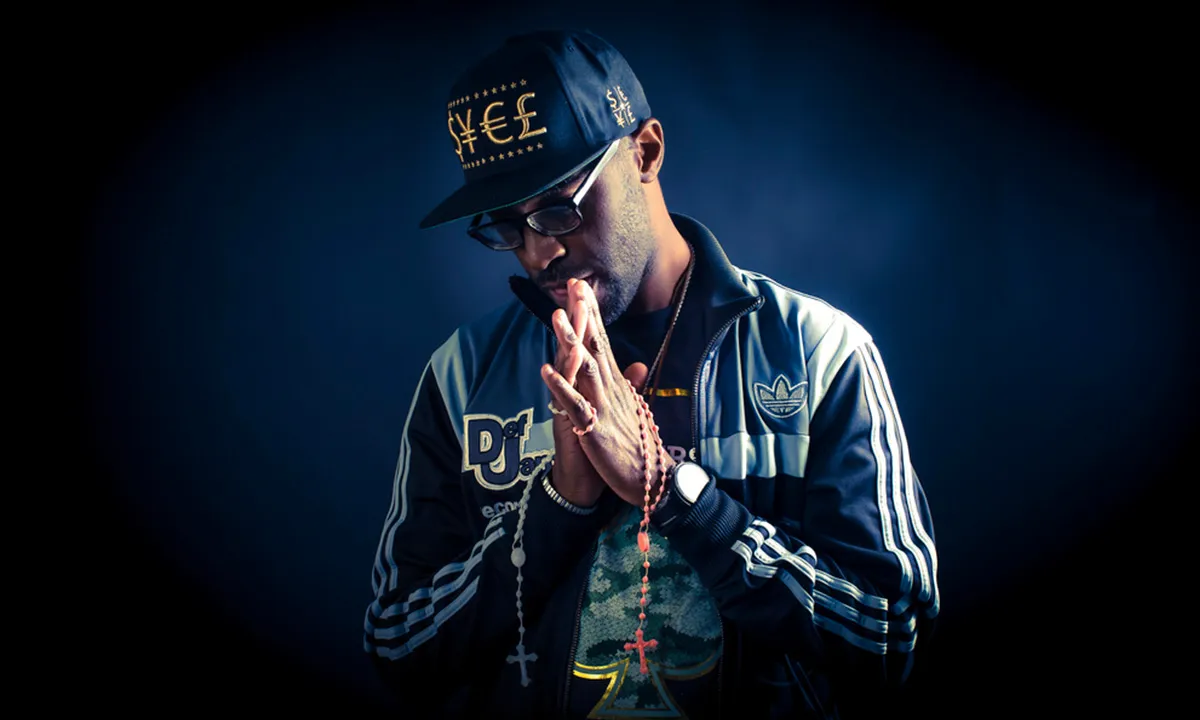 A male DJ poses in a praying position with gold chains