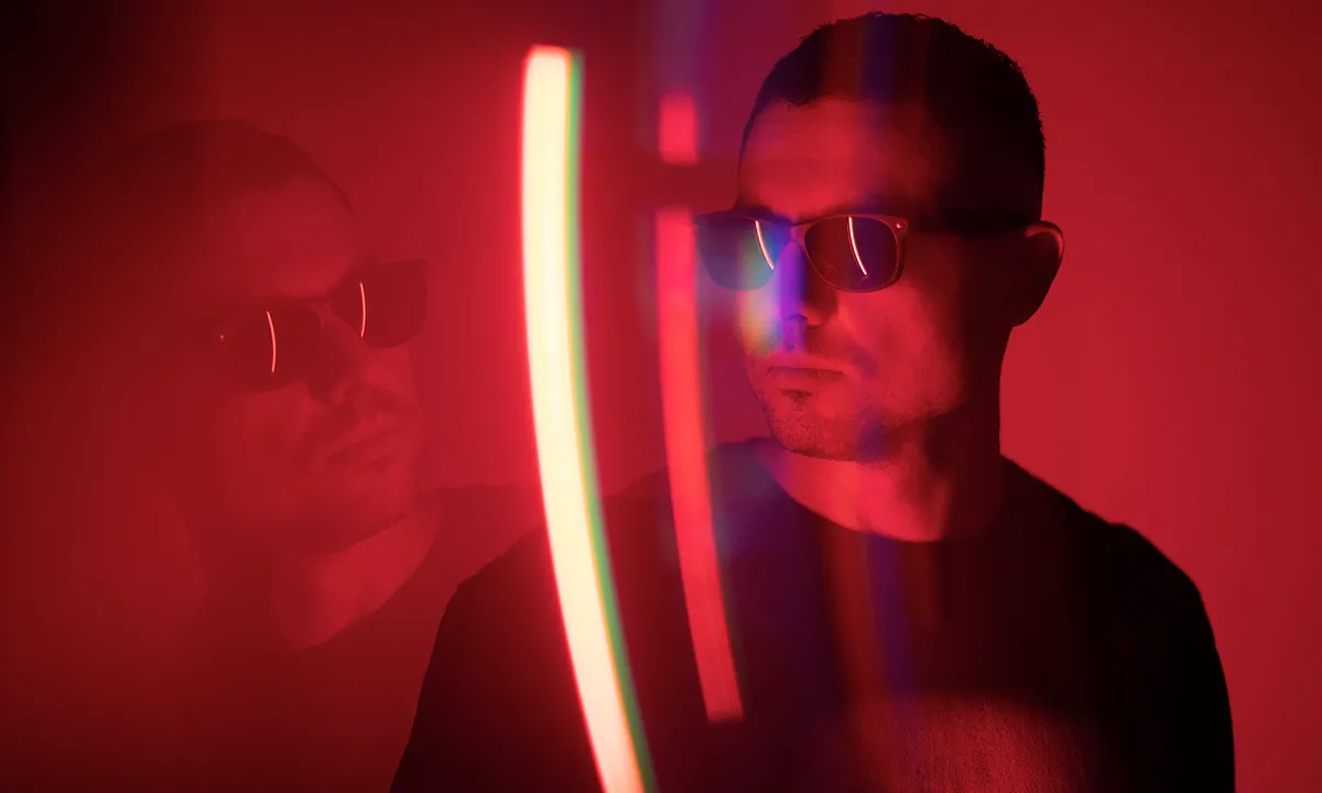 A male DJ wearing sunglasses gazing to the left in a striking DJ portrait