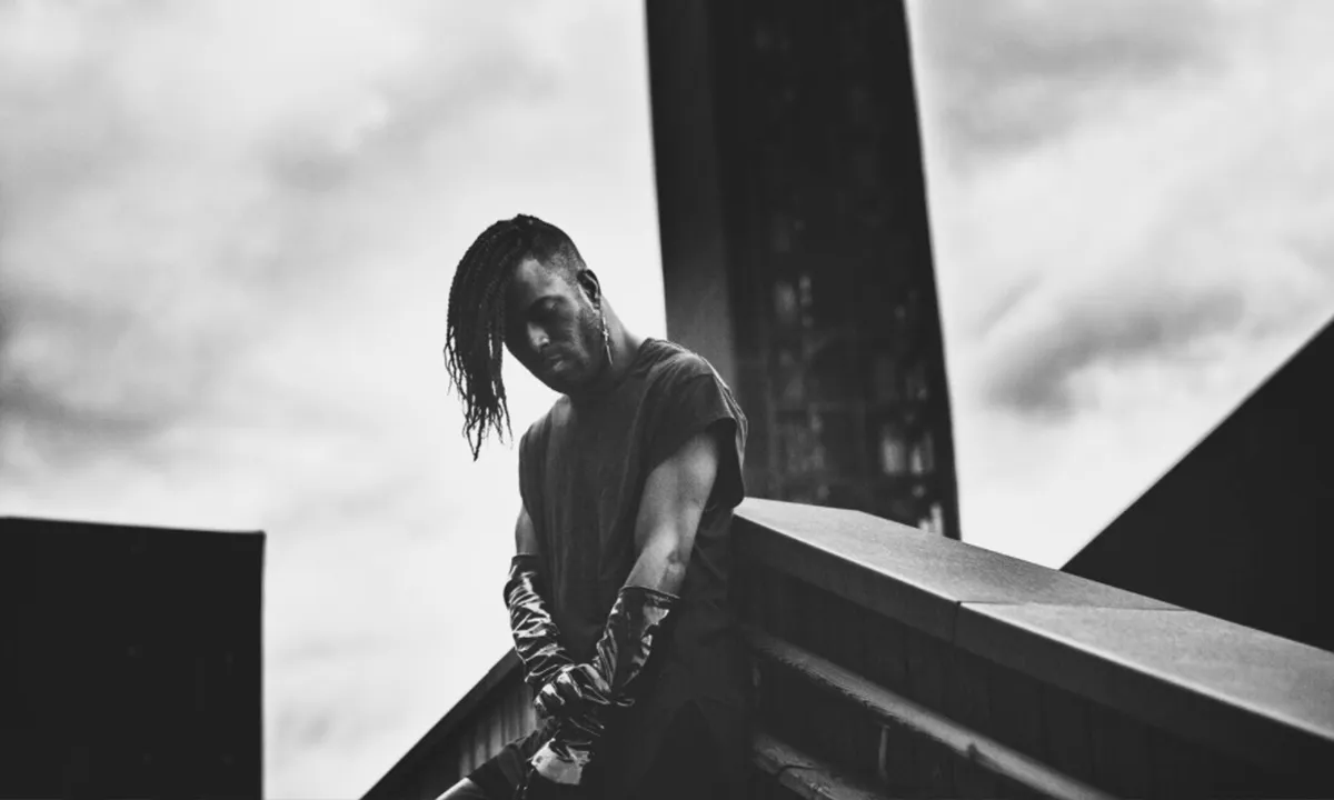 A moody black and white DJ photo against industrial architecture 