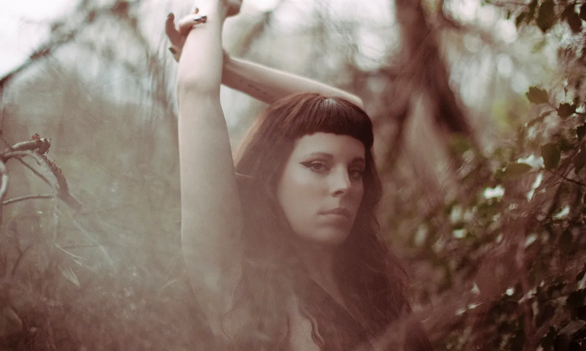 A moody and creative DJ photoshoot of a woman in a forest