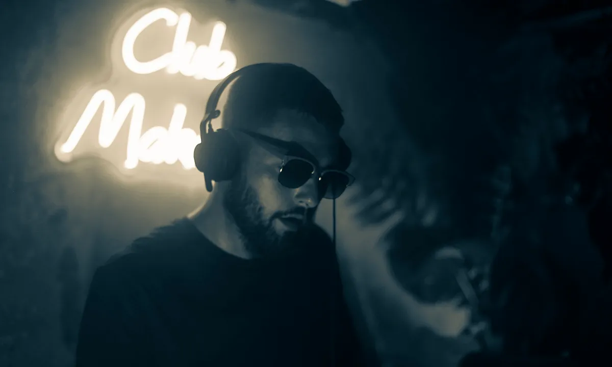 A cool DJ wears sunglasses in a dark club while he DJs