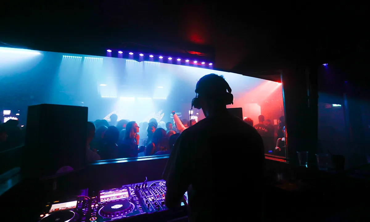 A DJ is performing in a large DJ booth at a superclub