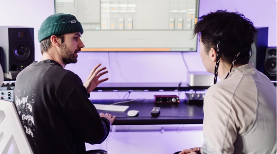 A producer teaches a new music production course student how to make music while sitting in a pro audio recording studio in London