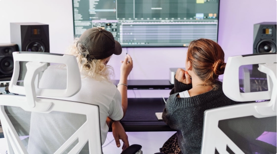 A producer teaches a new music production course student how to make music while sitting in a pro audio recording studio in London