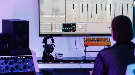 A producer teaches a new music production course student how to make music while sitting in a pro audio recording studio in London