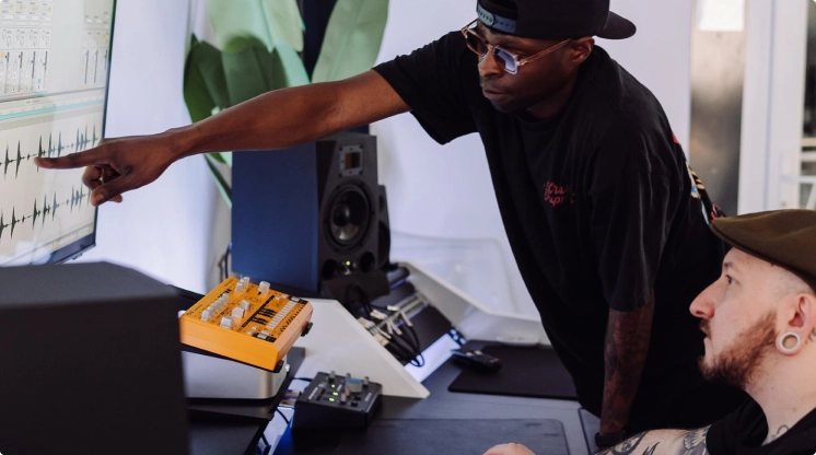 A producer teaches a new music production course student how to make music while sitting in a pro audio recording studio in London