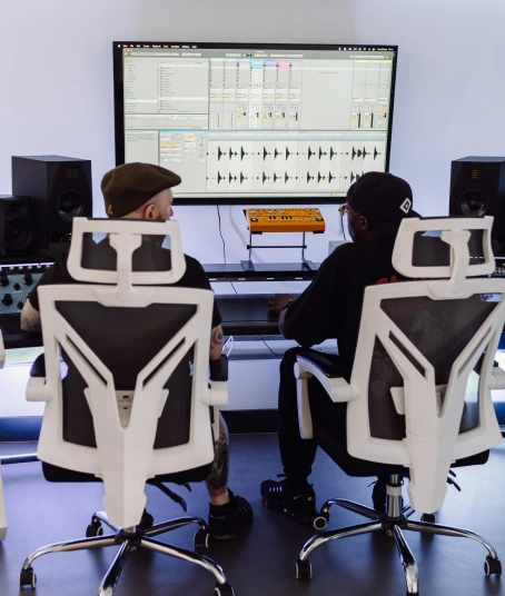 Two people sit at an impressive production desk in a recording studio