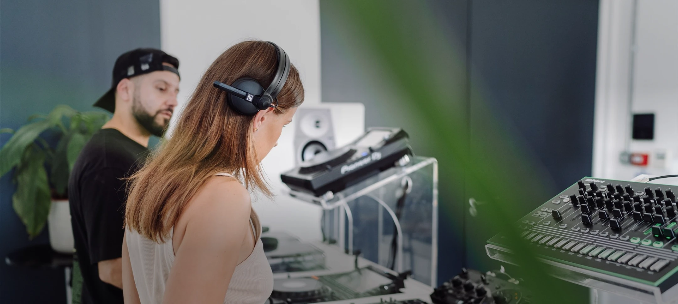 DJ tutor in a black cap watching a student in headphones mix on Pioneer CDJs at London Sound Academy.