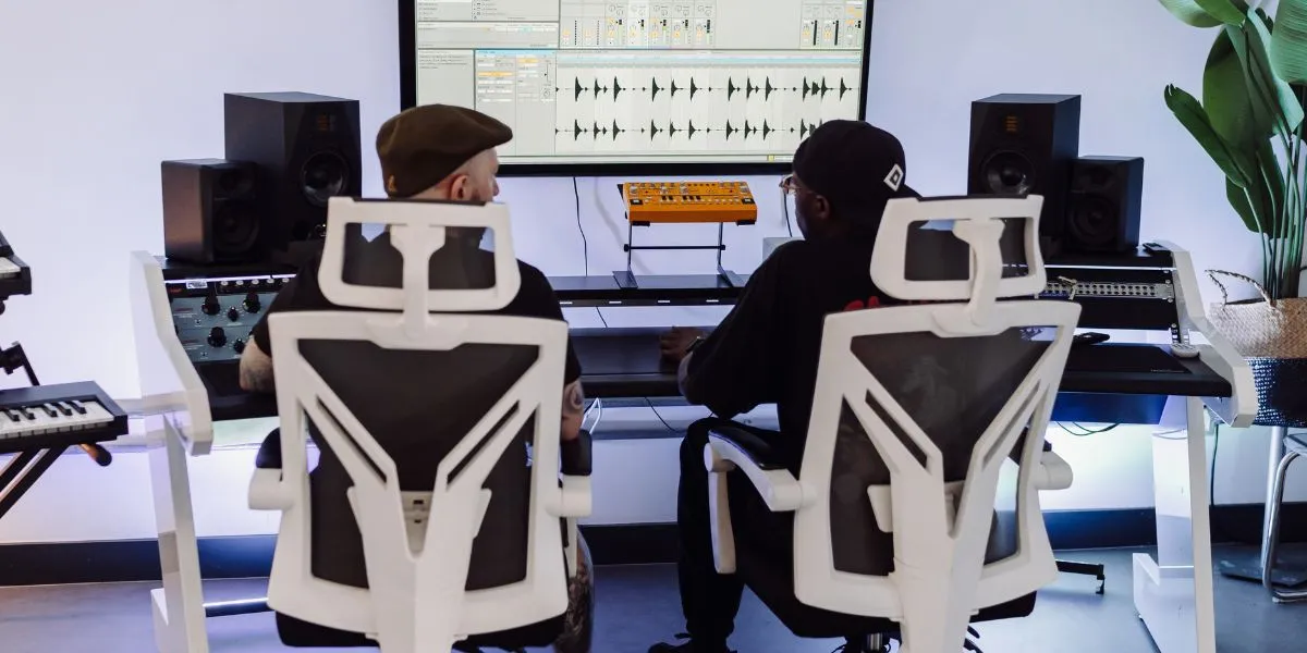 A music production tutor shows a student how to mix and master their track on a big screen