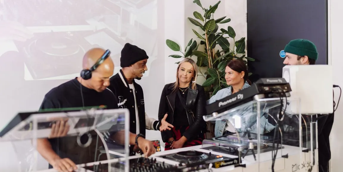 A woman is learning how to DJ behind a professional DJ booth at London Sound Academy