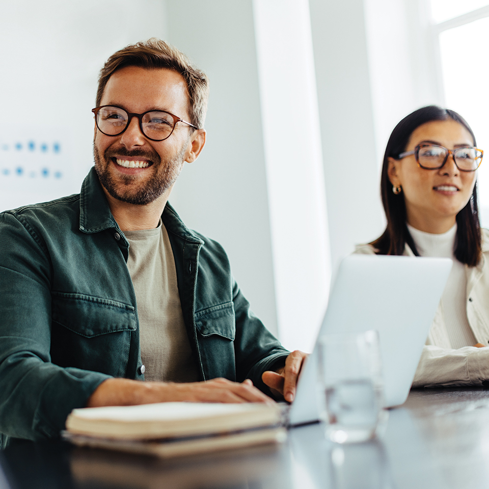 Two smiling people, business entrepreneurs, sitting at a desk with a laptop.
