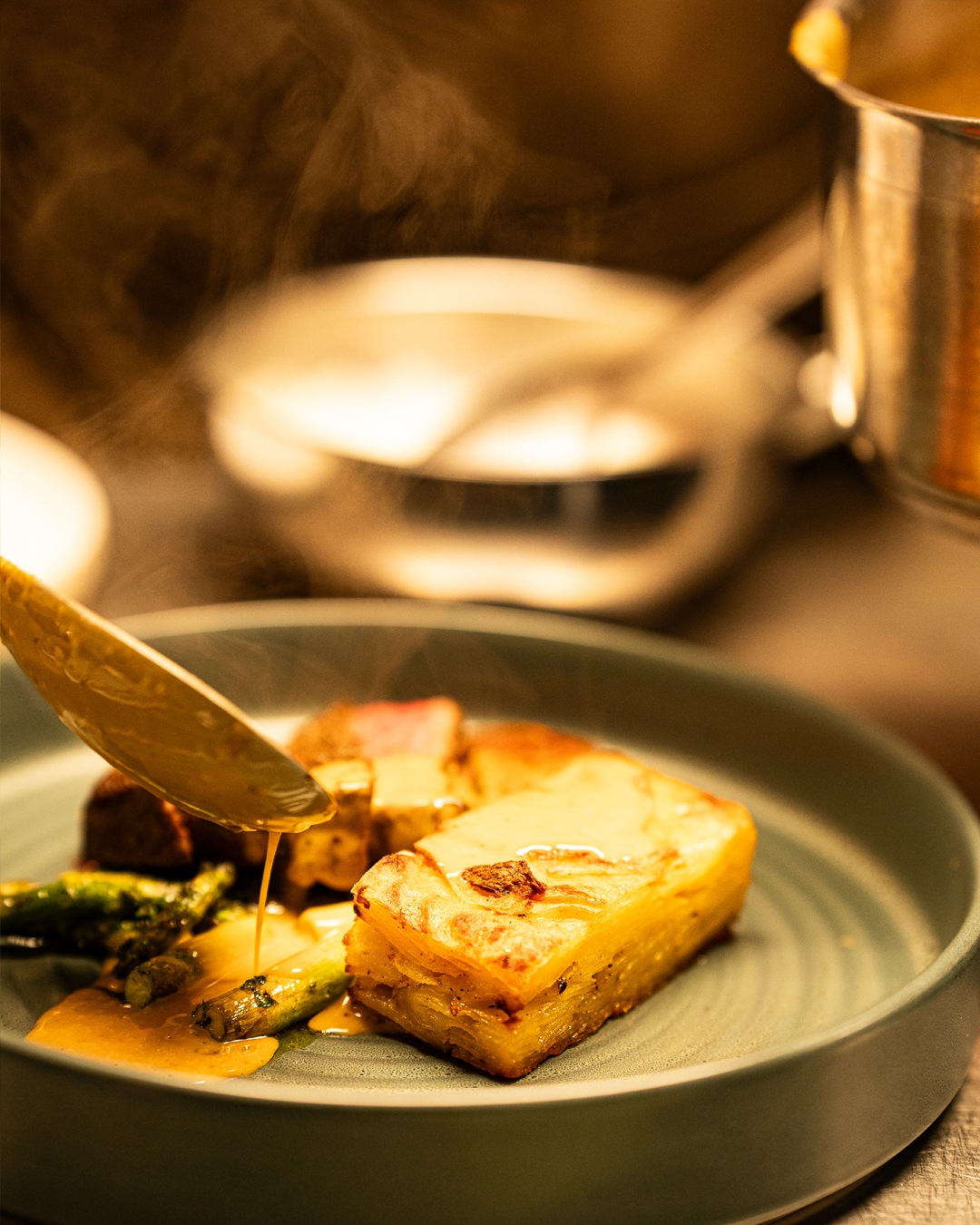 A picture showing a plate with hot food. A spoon is pouring sauce on top