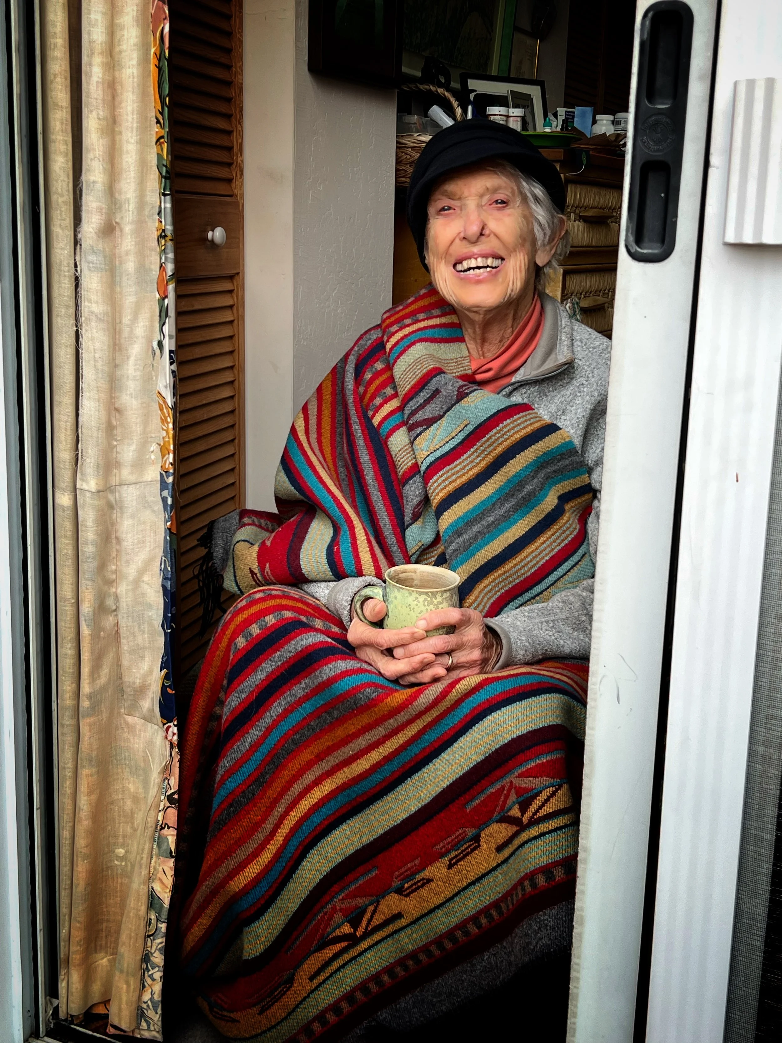 a photo of Joanna Macy wrapped by a blanket with a mug in her hand