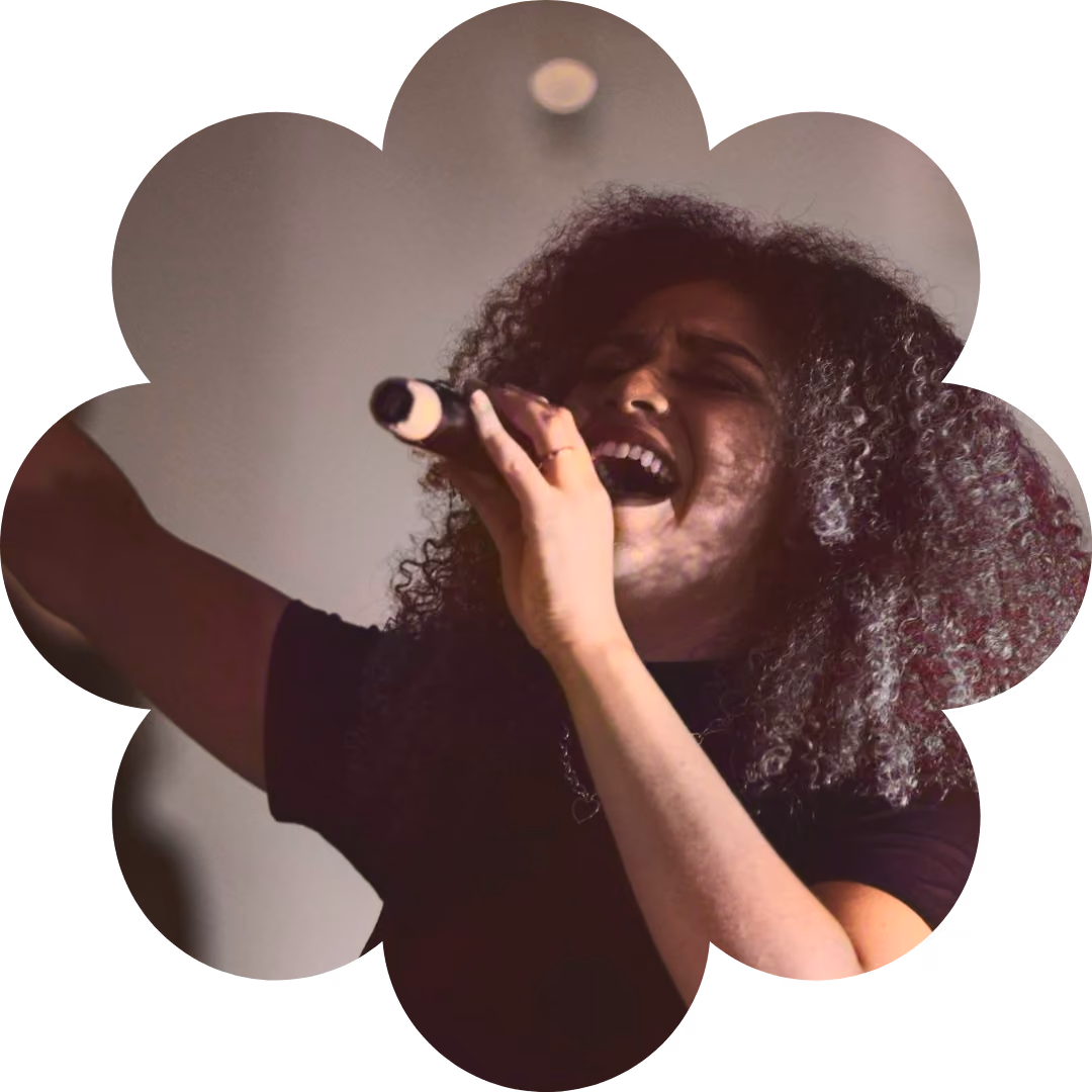 Woman with curly hair passionately singing into a microphone with eyes closed.