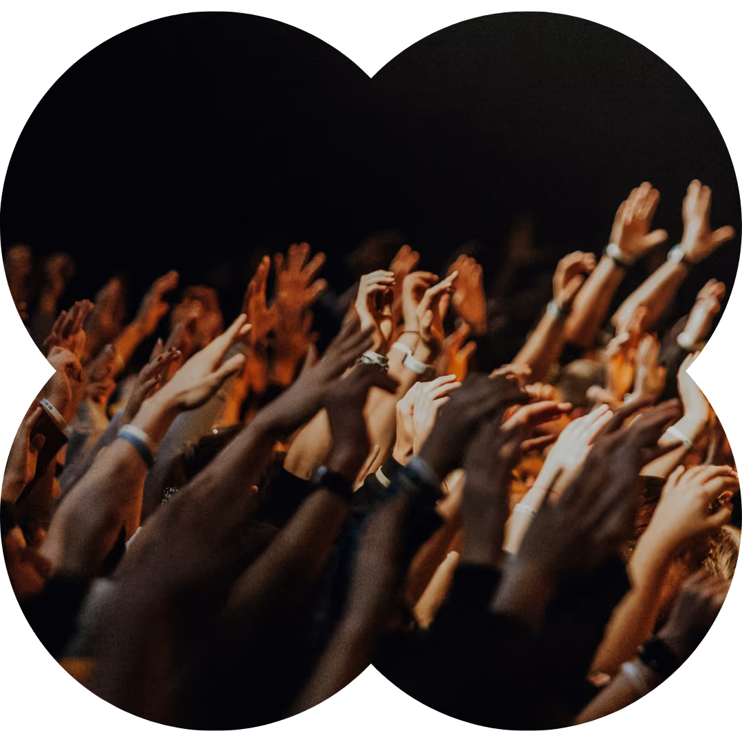 Multiple raised hands in a crowd with dark background at an event.