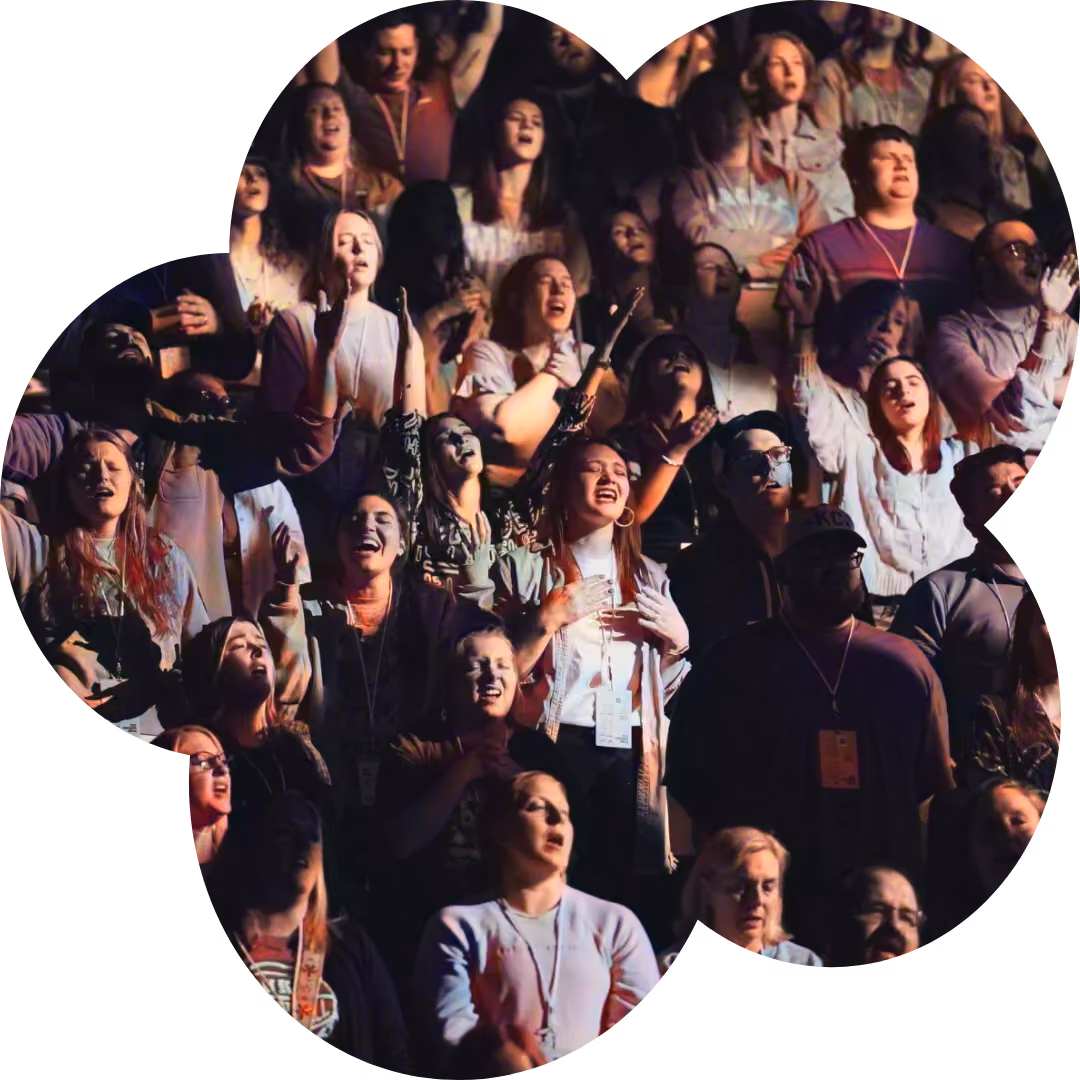 A diverse group of people singing together with eyes closed and hands raised.
