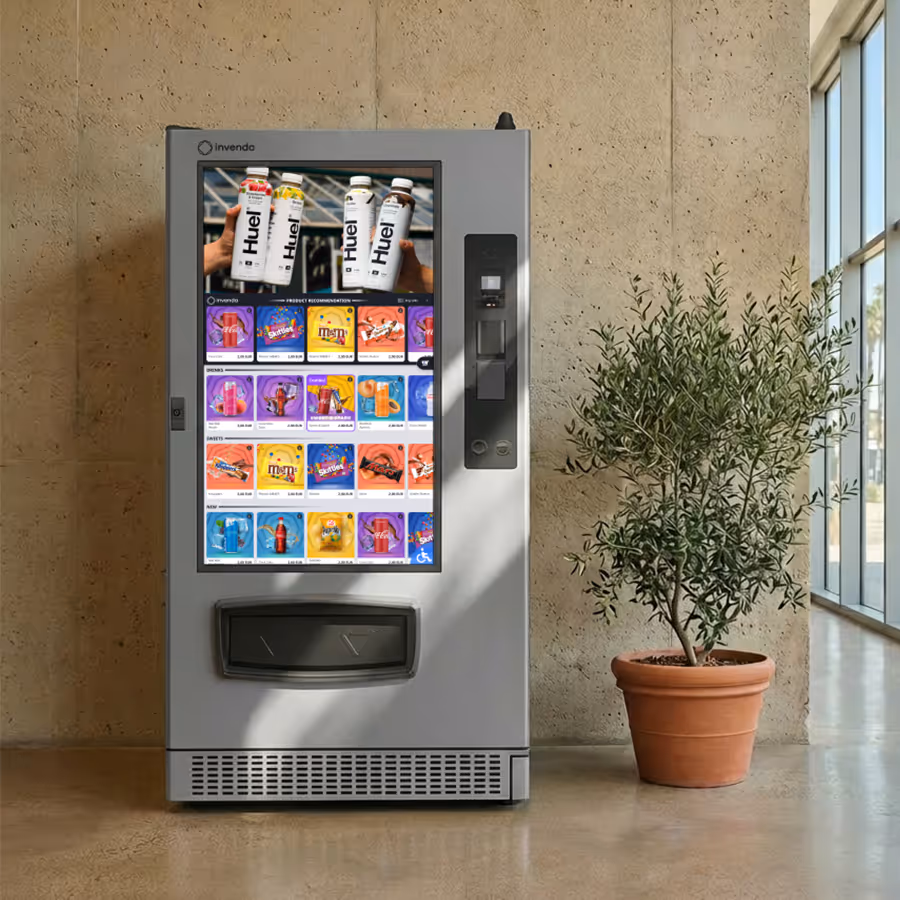 Modern Invenda vending machine with digital touchscreen displaying snacks and beverages, next to a potted green plant in a bright indoor space.