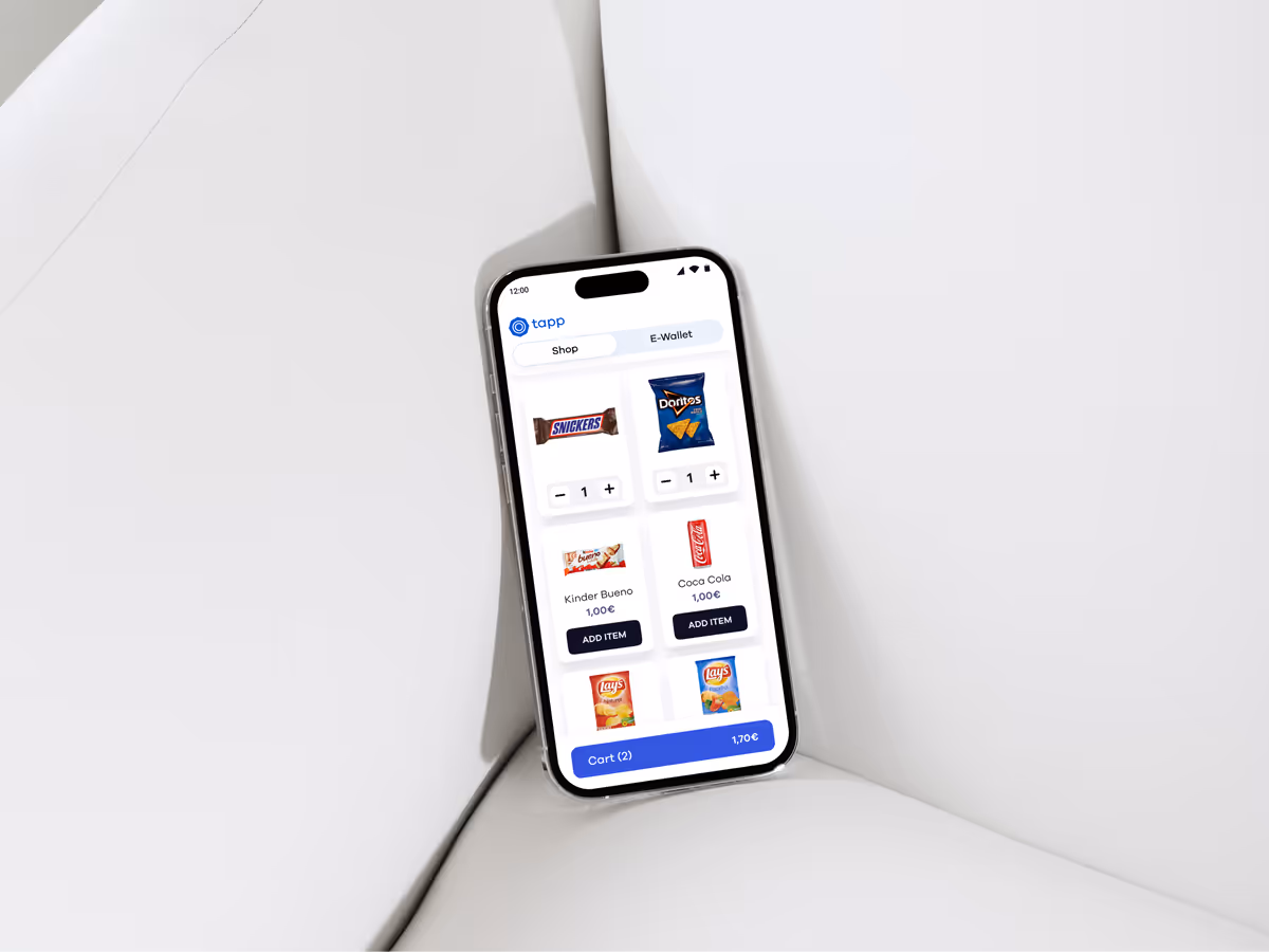 Smartphone displaying a vending app with snack items including Snickers, Doritos, Kinder Bueno, Coca Cola, and Lay's chips, showing prices in euros and a cart total.
