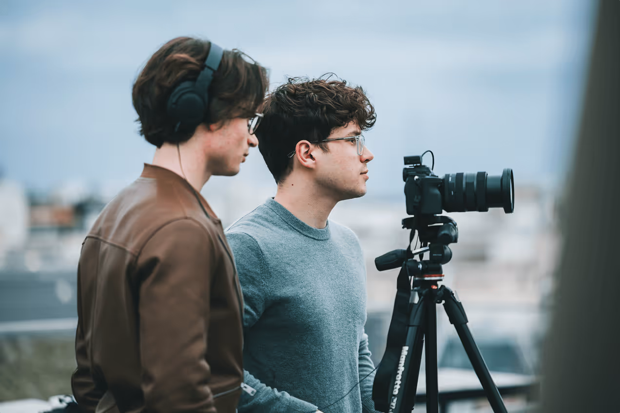 Deux jeunes hommes regardant à travers un appareil photo monté sur un trépied à l'extérieur.