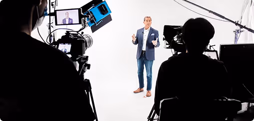 Une personne en costume debout dans un studio blanc, filmée par deux caméras avec des éclairages professionnels.