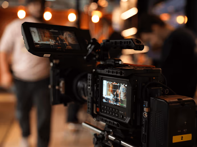 Caméra vidéo professionnelle avec écran affichant une scène floue en arrière-plan dans un environnement intérieur chaleureux.