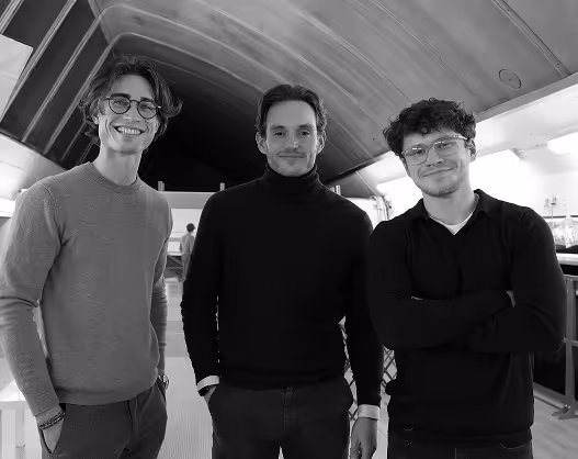 Trois jeunes hommes debout sous un plafond voûté, souriants et posant pour la photo.